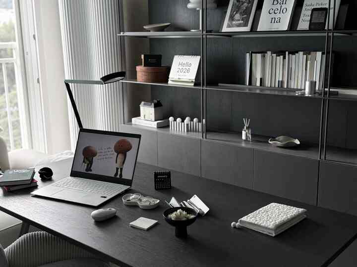 ダークグレー調のモダンなホームオフィス空間、机と本棚が配置され、ノートパソコンとランプが置かれている印象的なインテリア