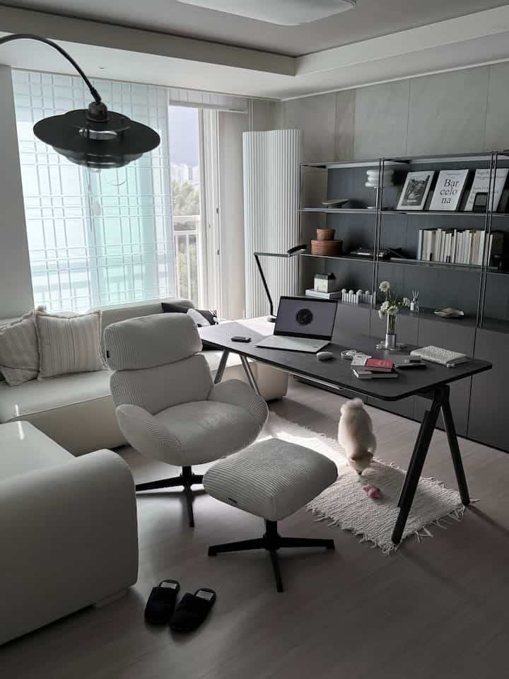 白とグレーのナチュラルモダンのホームオフィス、デスク、ソファ、アームチェアが配置された落ち着いた作業空間