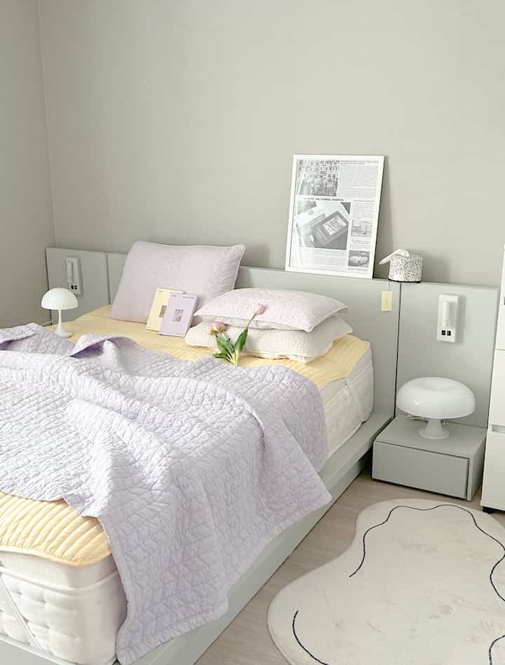 ライトグレーの色調の子供部屋の寝室、パステルパープルの布団カバーとナイトテーブルが配置された温かみのあるインテリア