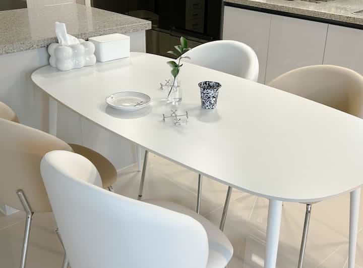 ホワイトとシルバーのトーンが映えるコンパクトなダイニング、4人用の楕円形ダイニングテーブルと椅子が配置された清潔感のあるモダンな空間