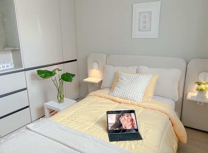 ナチュラルな色調の寝室、枕と黄色いブランケットを置いたベッドとフロアランプがある落ち着いた空間