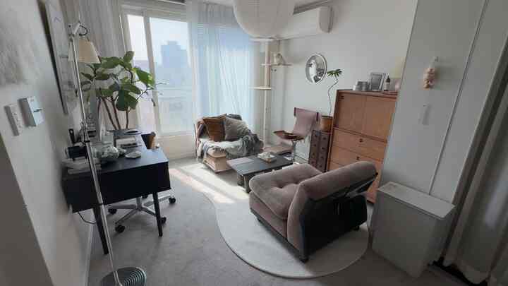 白と茶色のトーンが特徴的な小さなリビング、中央にソファとアームチェア、窓際にキャットタワーが置かれた雰囲気のある空間