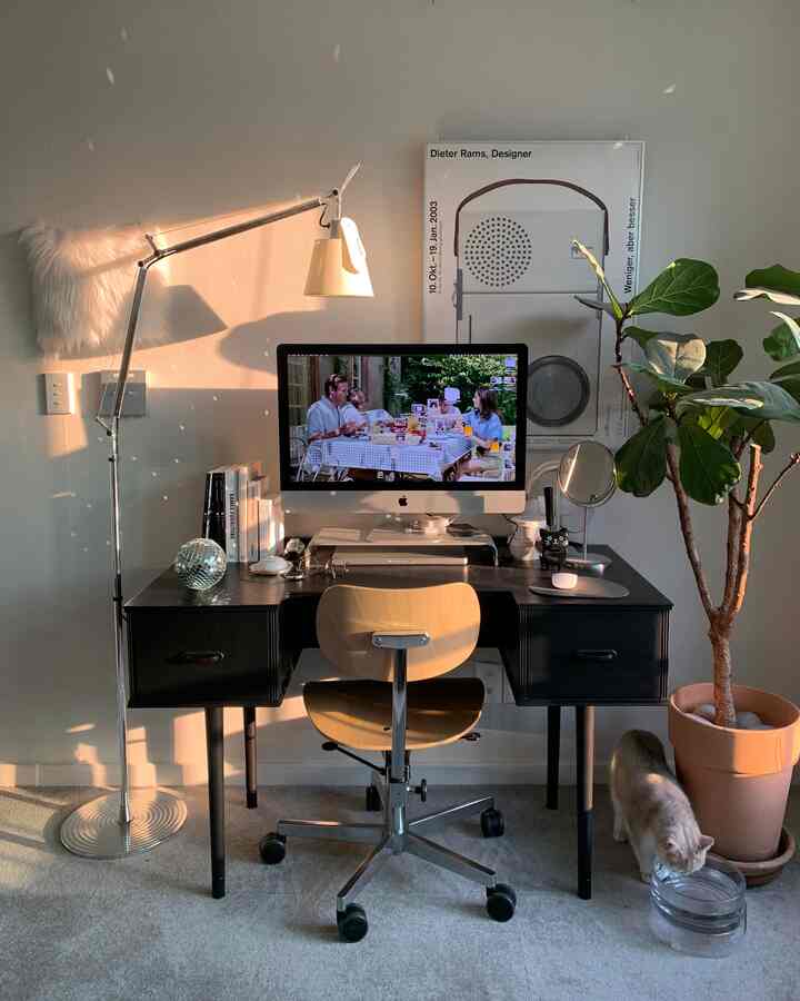 黒いデスクと木製のオフィスチェア、フロアランプ、観葉植物、猫がいる明るいホームオフィスのインテリア