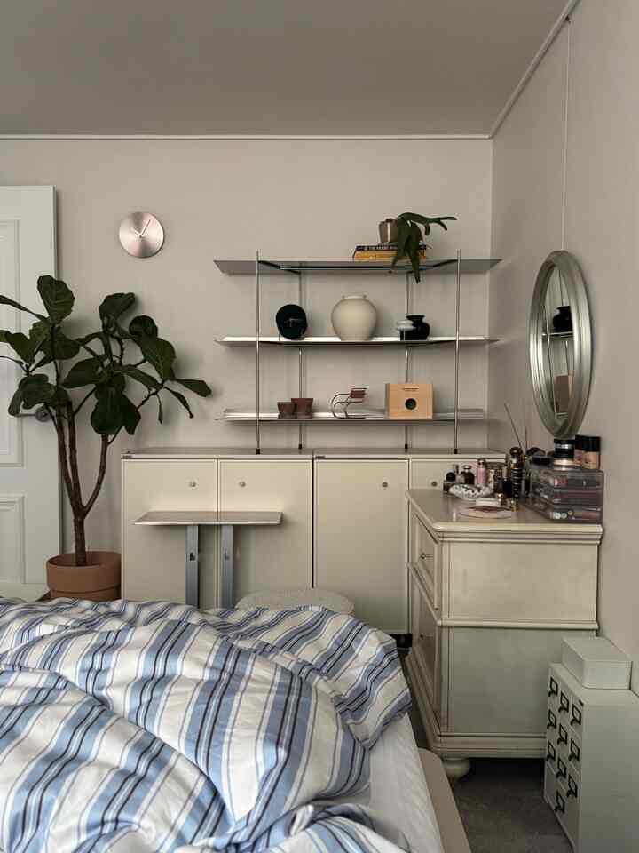 ホワイトトーンの寝室で、ブルーストライプの寝具と観葉植物、キャットハウスが配置された雰囲気のあるインテリア