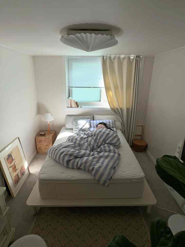 白とナチュラルカラーの寝室、中央にクイーンサイズのベッドが配置され、ブラインドとカーテンが窓を覆う落ち着いたインテリア