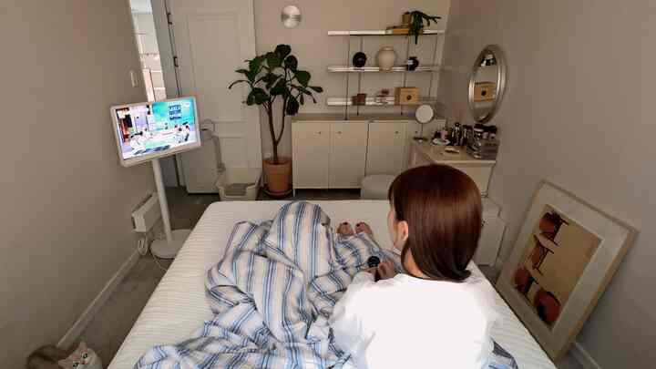 白とグレーのトーンの狭い寝室、中央にベッドと壁掛けテレビ、ペットの猫がいるウォークインクローゼットのある空間