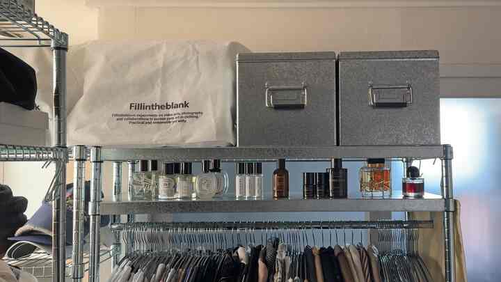 ナチュラルカラーのワンルーム、金属製の棚とハンガーラックに衣類と香水が整然と配置された収納スペース