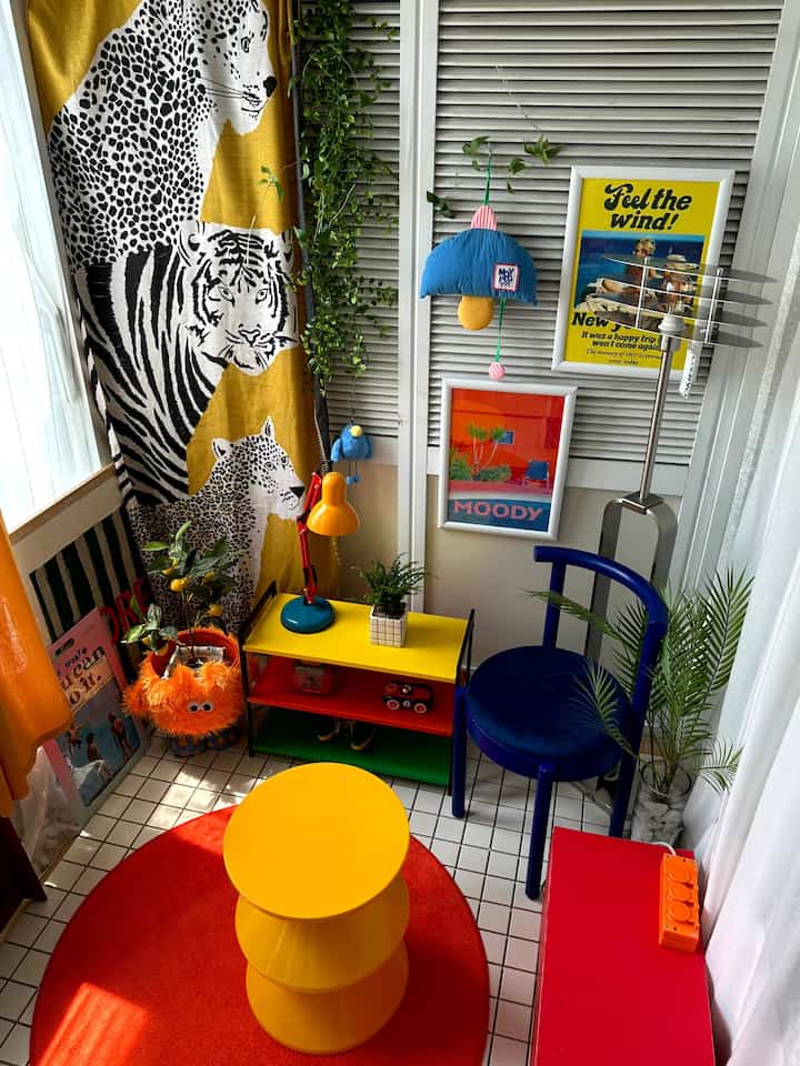 黄色と赤の鮮やかな小さな部屋、丸い黄色のスツールと青い椅子、多彩な小物とフロアランプが配置された印象的な空間