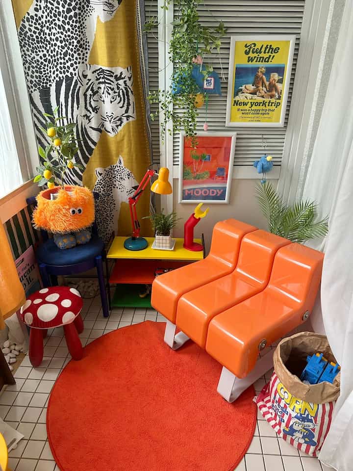 オレンジと赤のトーンの小さな部屋、ユニークなソファ、子供用スツール、植物とポスターが配置された雰囲気のあるインテリア