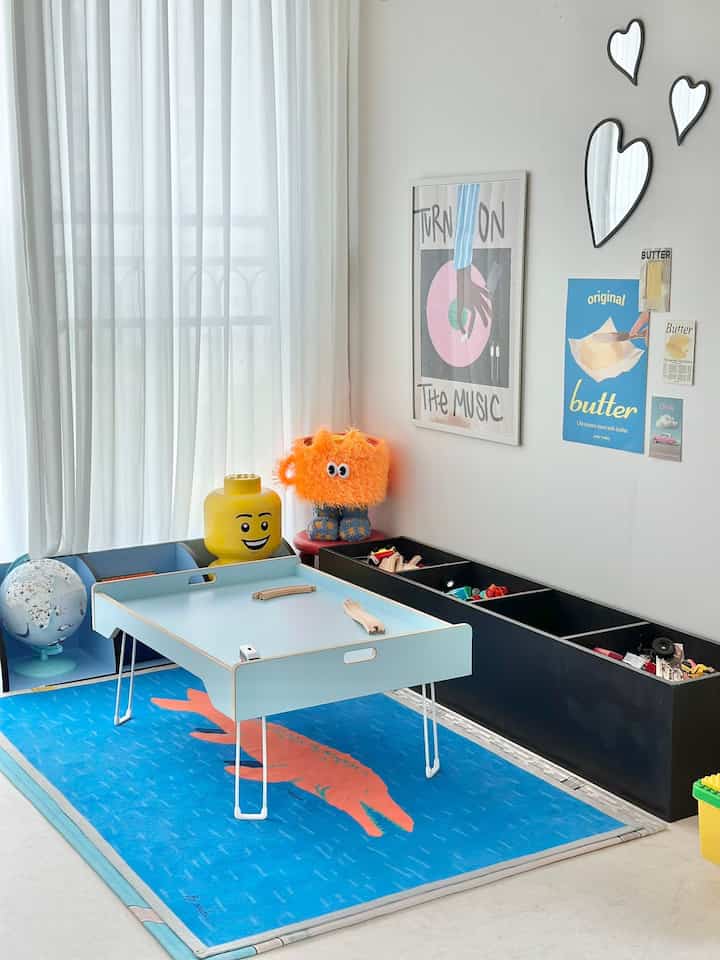 明るい白い壁とカーテンの子供部屋、青いラグと低い机が配置された北欧風の印象的な空間