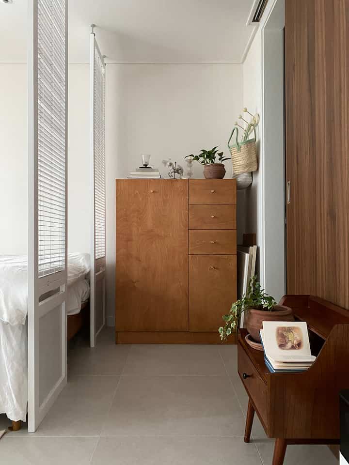 ナチュラルな色調の寝室、木製のワードローブとパーティションスクリーンが配置された落ち着いた雰囲気のインテリア