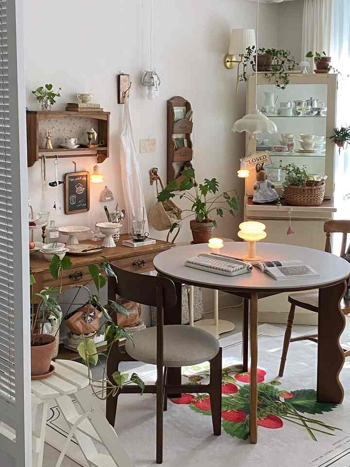 白い壁とナチュラルな木目調家具が調和する内装、ダイニングテーブルと椅子、多くの植物が雰囲気のある空間を演出している