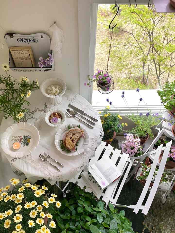 ホワイトとナチュラルカラーのベランダ、植物と折りたたみ椅子、レースのテーブルクロスが温かみのある雰囲気を演出