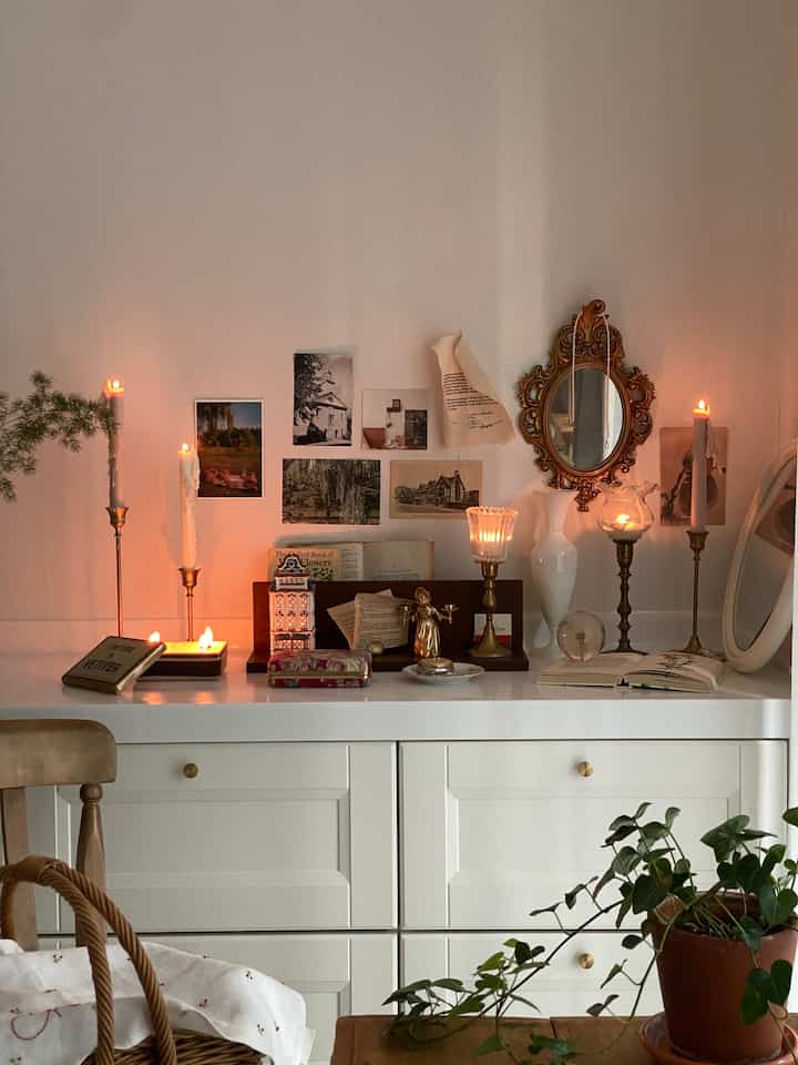 温かみのある灯りのキャンドルとヴィンテージの装飾品が置かれた白いキャビネットがある心地よいリビング