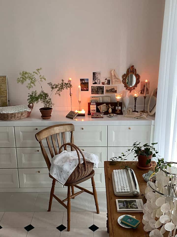 アイボリーの壁と木目調家具、ドレッサーの上にはヴィンテージの小物とキャンドルが配置された自然な雰囲気のホームオフィス空間