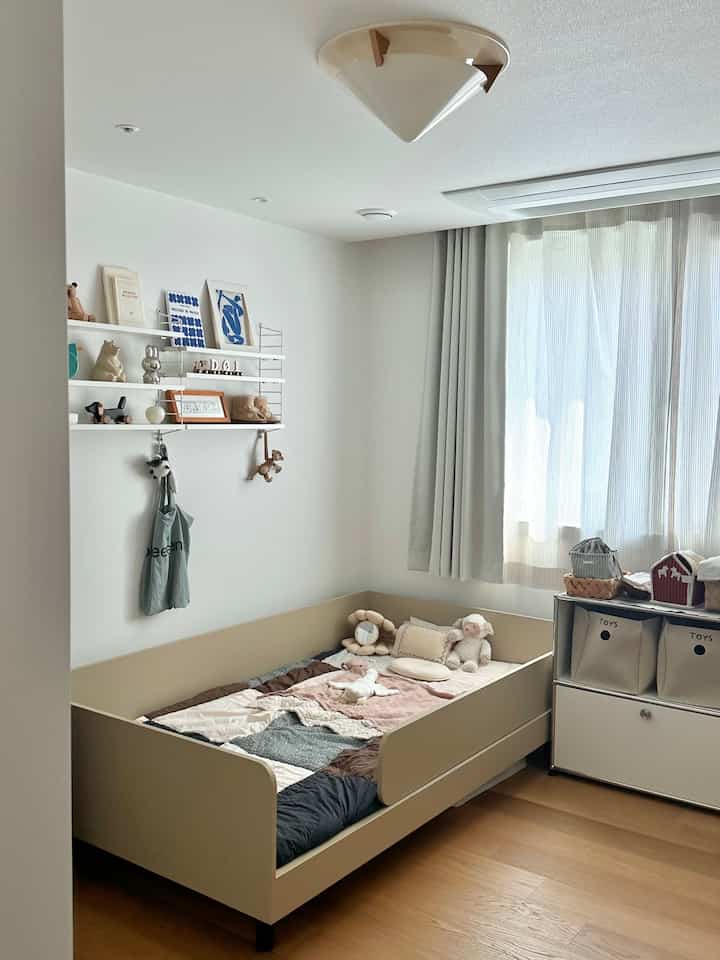 ナチュラルカラーとホワイトの子供部屋、ベージュのベビーベッドと収納が配置された落ち着いたインテリア