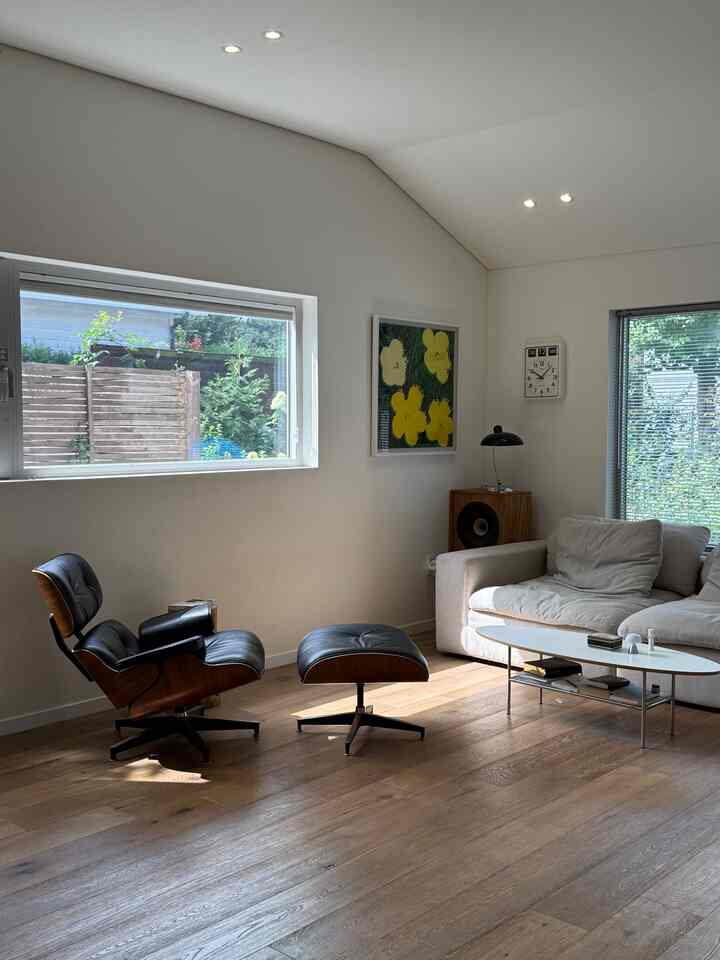 ナチュラルな木目調と白を基調としたリビング、イームズのラウンジチェアとアイボリーのソファが配置されたモダンで落ち着いた雰囲気のインテリア