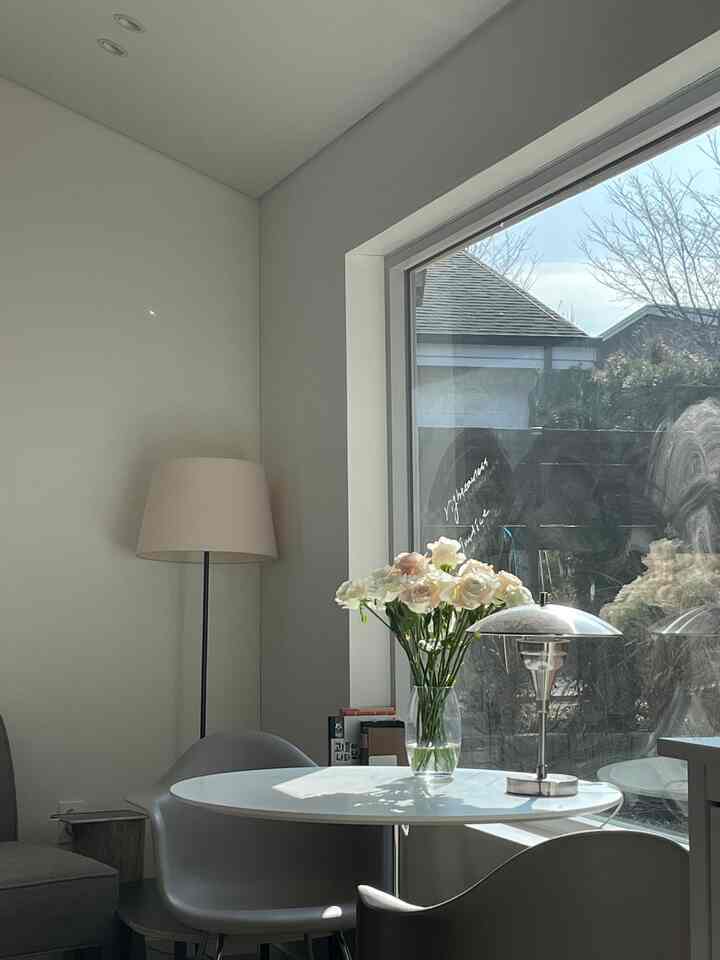 ホワイトとグレーのトーンが特徴のキッチン兼リビング、丸テーブルとアームチェア、フロアランプが配置された雰囲気のあるナチュラルモダンなインテリア