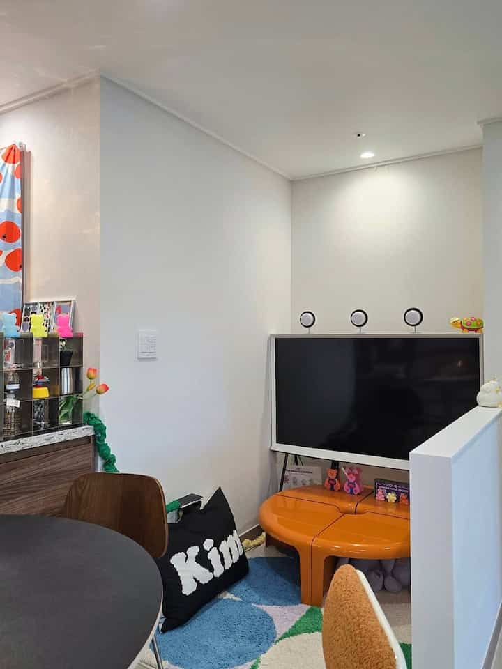 白い壁とオレンジのテーブルが配置されたリビング、テレビとミニマルな小物が印象的な空間