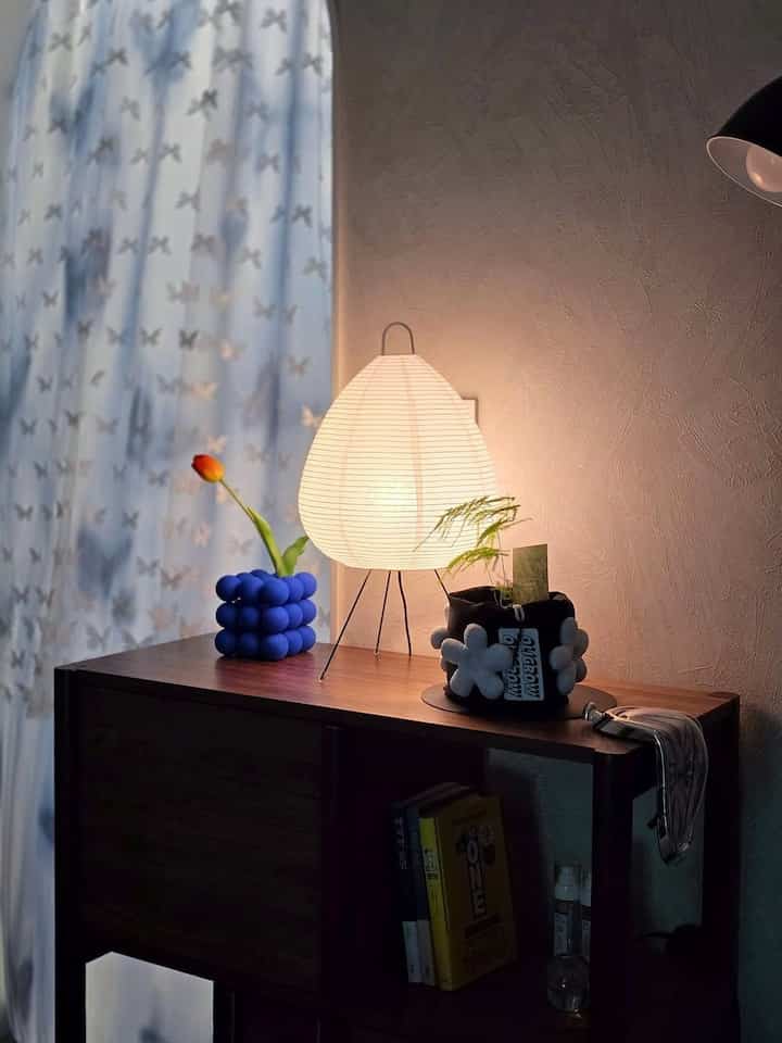 白いカーテンと茶色の木製収納棚、暖かい照明が配置されたナチュラルなコーナー空間