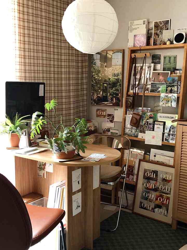 白い照明と木目調のダイニングテーブルがあるカフェ風の書斎兼ホームオフィス空間。壁面にポスターや植物が配置された雰囲気のあるインテリア