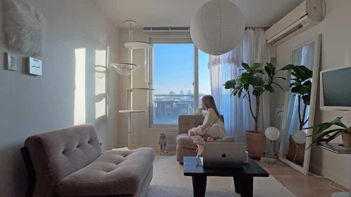 明るいホワイトとナチュラルブラウンのトーンのリビング、キャットタワーとソファが配置された落ち着いたモダンな空間