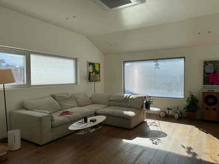 明るい白と木目調が調和したリビング、アイボリーのコーナーソファと大きな窓、植物が配置された雰囲気のある空間