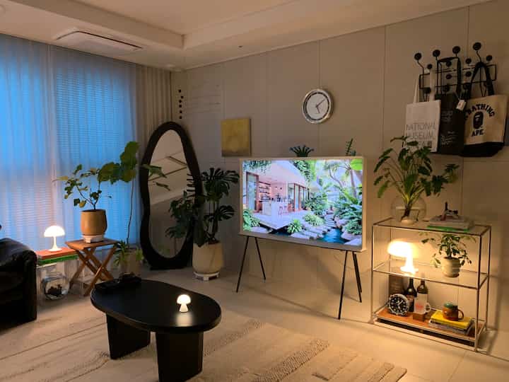白と黒のトーンが特徴のリビングルーム、大型の鏡とテーブルランプ、植物が配置された雰囲気のあるホームギャラリー空間