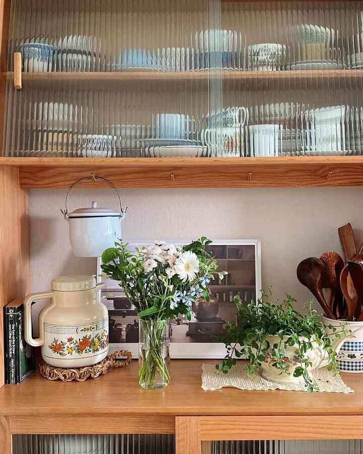 ナチュラルな木目調のキッチン収納棚と花瓶、植物が配置された温かみのあるキッチンスペース