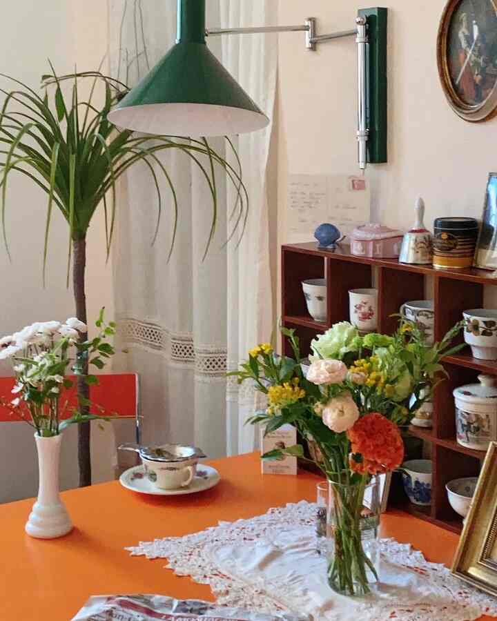 鮮やかなオレンジ色のテーブルと緑色の照明が印象的なダイニング、花瓶と植物が配置された温かみのあるインテリア