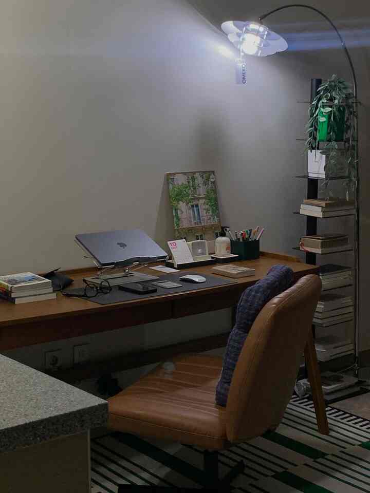 グレーの壁とウッドトーンの机が置かれた一人用ナチュラルモダンな書斎、落ち着いた雰囲気のフロアランプと本棚が配置された空間