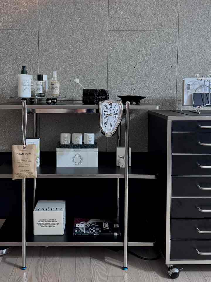 グレーの壁とスチール棚、黒いチェストが配置されたミニマルでインダストリアルな印象の小さなショールーム空間