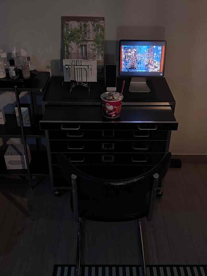 暗い照明の中、黒を基調としたホームオフィス空間に黒いデスクとチェアが配置され、アイパッドスタンドとアイスクリームカップが置かれている印象的なインテリア