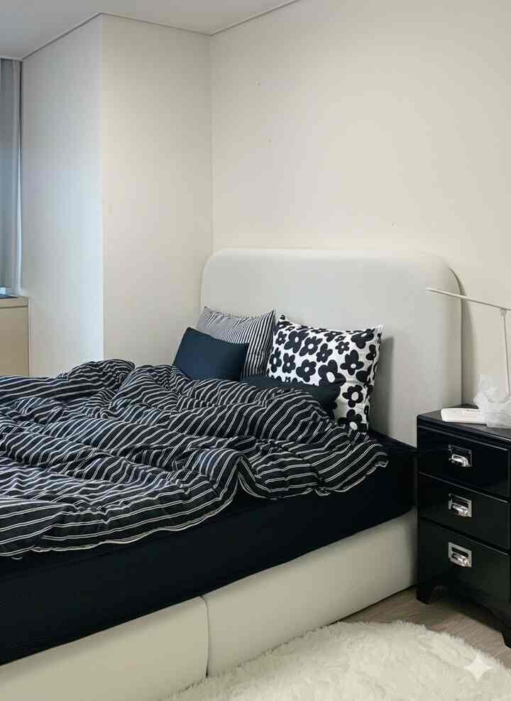 白い壁と黒い寝具が調和したモダンな寝室、中央に大きなベッドとナイトテーブルが配置された印象的な空間