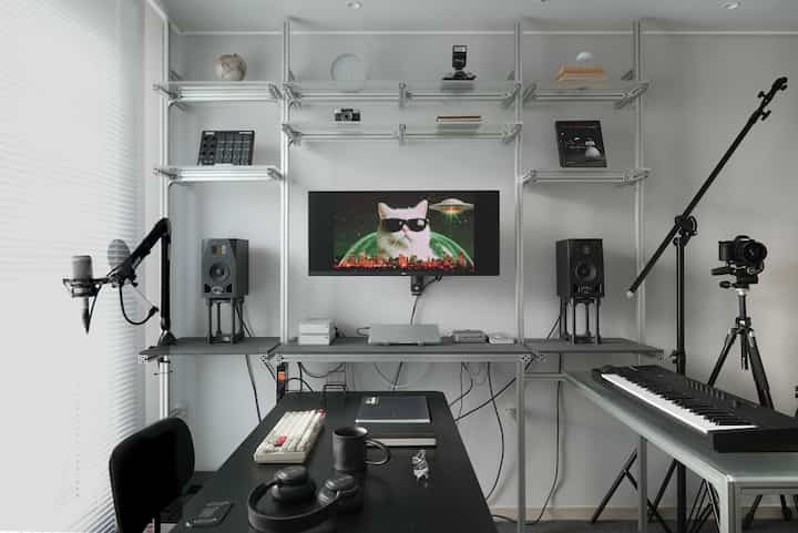 モノトーンの一人暮らし用ホームオフィス、デスクや音楽キーボード、スピーカー、マイクが配置された現代的な作業スペース