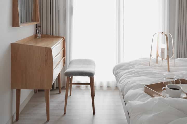 ナチュラルな木目調と白いカーテンが調和した寝室、化粧台とスツールが配置された印象的な空間