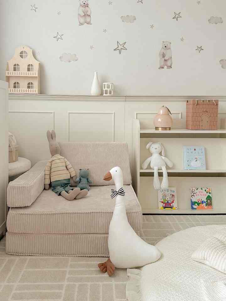 ベージュとクリーム色調の子供部屋、柔らかな曲線のファブリックソファと丸いクッションが配置された温かみのある北欧風インテリア