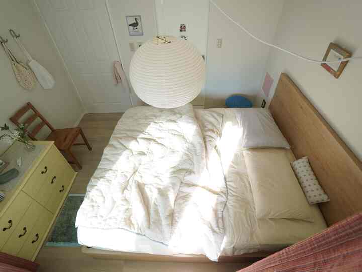 ナチュラルな木目調と白を基調とした6畳の寝室、丸いペンダントライトとシンプルな家具が配置された雰囲気のあるインテリア