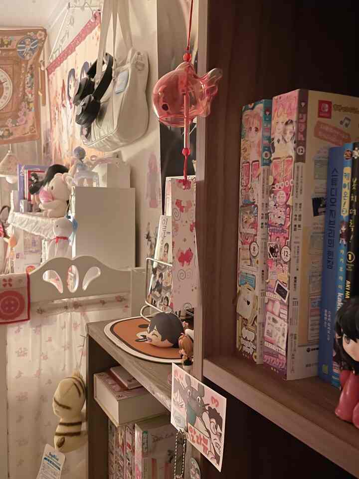 ナチュラルな色調の壁と本棚が配置された部屋、可愛らしいアニメグッズと透明なガラス風鈴が調和する雰囲気のあるインテリア