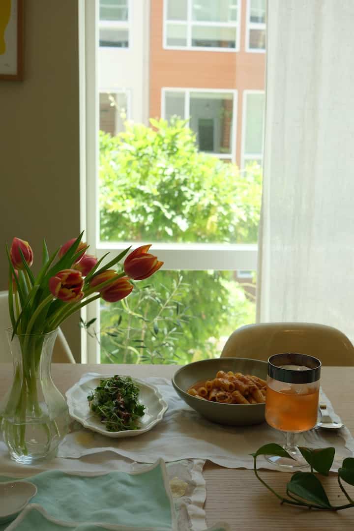 自然光の入るナチュラルカラーのキッチンダイニング、中央に花と食卓が置かれた雰囲気のある空間