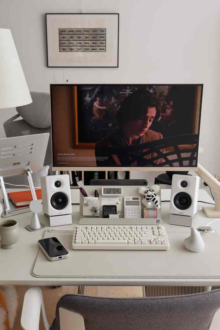 白とベージュのトーンのホームオフィスデスクゾーン、モニターやキーボード、スピーカー、ランプが整然と配置された印象的な空間