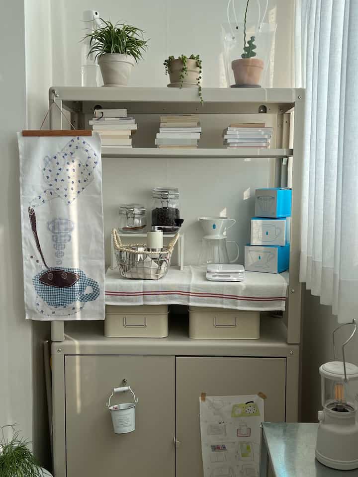 白とベージュのトーンの棚にコーヒー用品と植物が整頓された、落ち着いた印象のホームカフェ空間