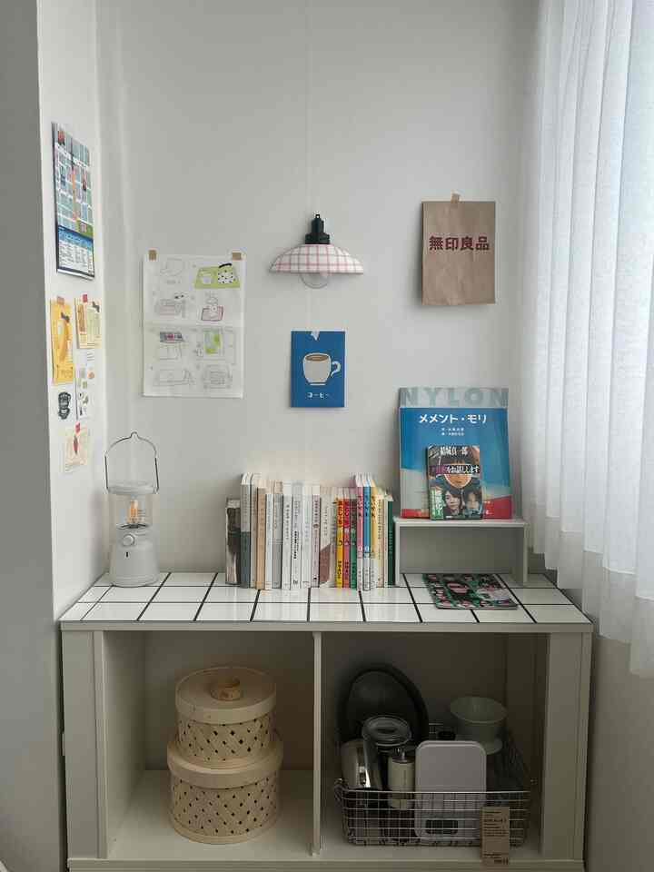 白とナチュラルトーンの小さい部屋、北欧風の本棚や壁のポスター、柔らかい照明が配置された空間