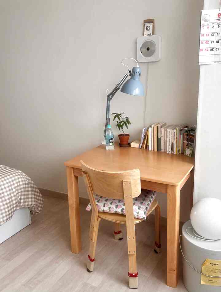 白と木目調が調和する寝室の小さな部屋、シンプルな机と椅子、デスクランプと本が配置された落ち着いた空間
