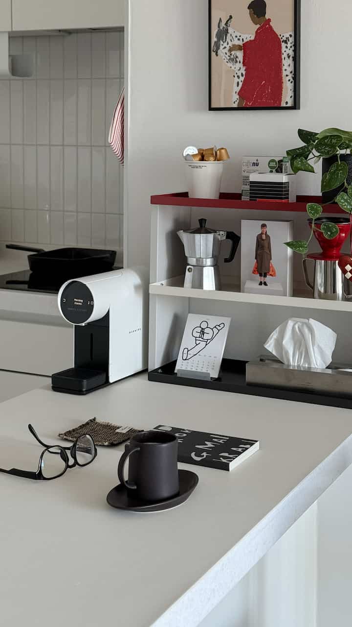 白と赤のトーンが特徴的なモダンなキッチン空間、カプセルコーヒーマシンとコーヒーアクセサリーが配置された清潔感のあるおうちカフェ