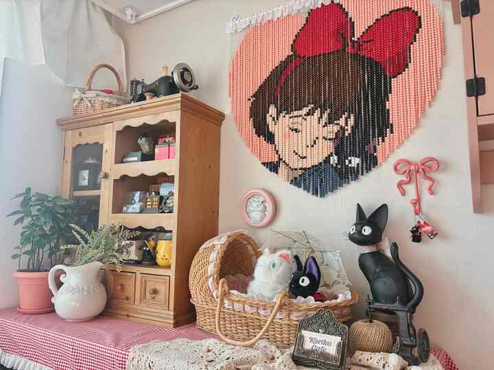 ベージュとピンクの色調のかわいらしいインテリア空間、キキのキャラクターオブジェとヴィンテージ風の木製収納棚が配置された温かみのあるインテリア
