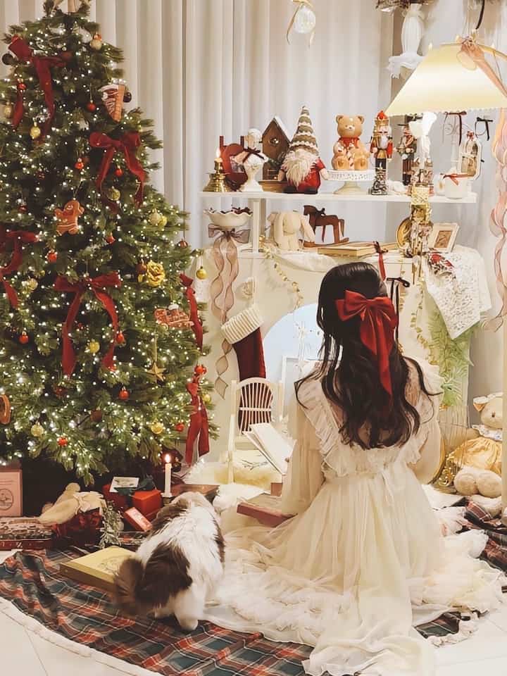 ホワイトとレッドの色調のリビング、クリスマスツリーと装飾品が配置され、猫と女性が座る温かみのある雰囲気のインテリア