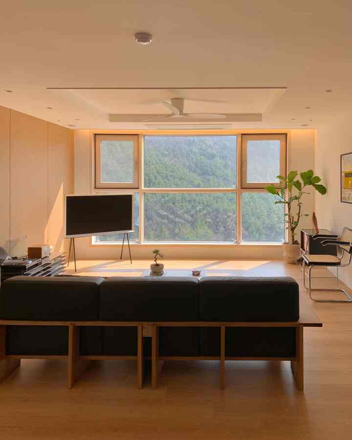 木目調とホワイトのトーンのリビングルーム、大きな窓とソファ、テレビが配置された雰囲気のあるナチュラルモダンな空間