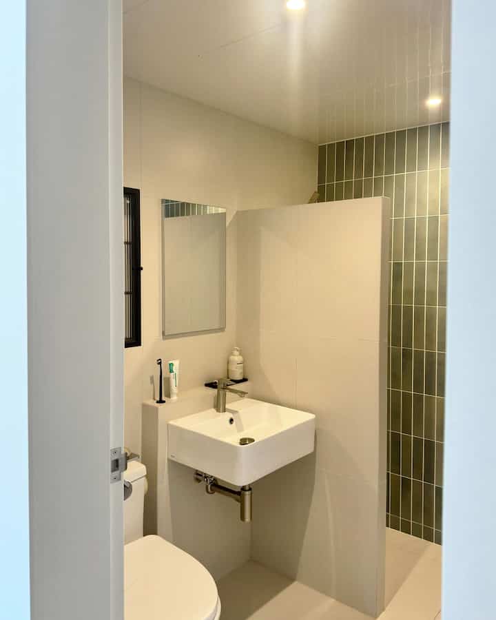 白とグリーンタイルが調和するバスルーム空間、洗面台と壁掛け鏡、トイレが配置された清潔感あるモダンなインテリア