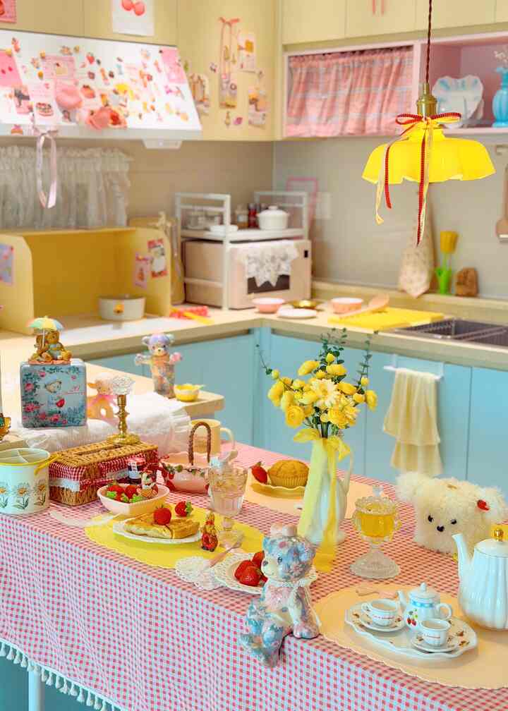 黄色とピンクの色調のキッチン、かわいい飾りとチェックのテーブルクロスが配置された雰囲気のあるおうちカフェのインテリア